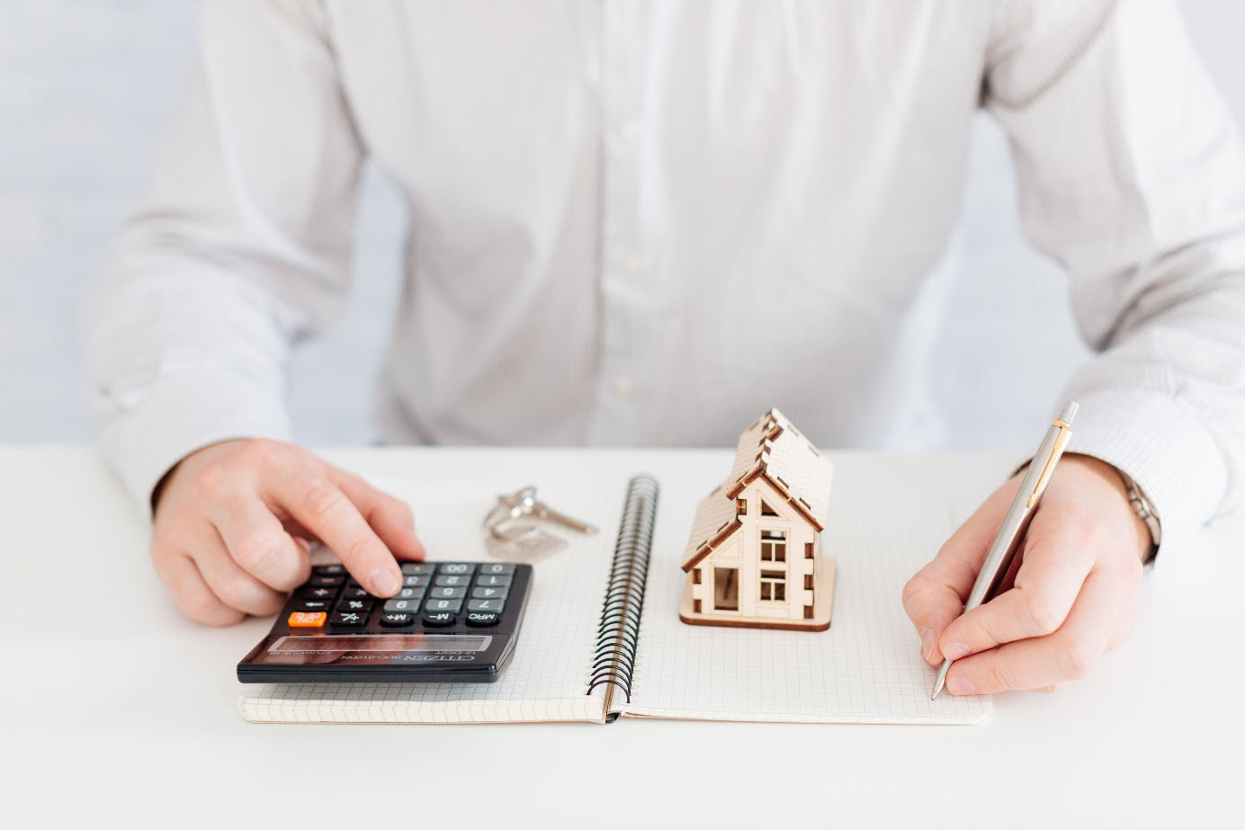 Un homme en chemise blanche assis à son bureau prêt à noter ses calculs pour son prêt immobilier.